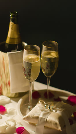 Vertical-Video-Of-Table-Set-To-Celebrate-Marriage-With-Champagne-And-Rings-On-Satin-Cushion-At-Night